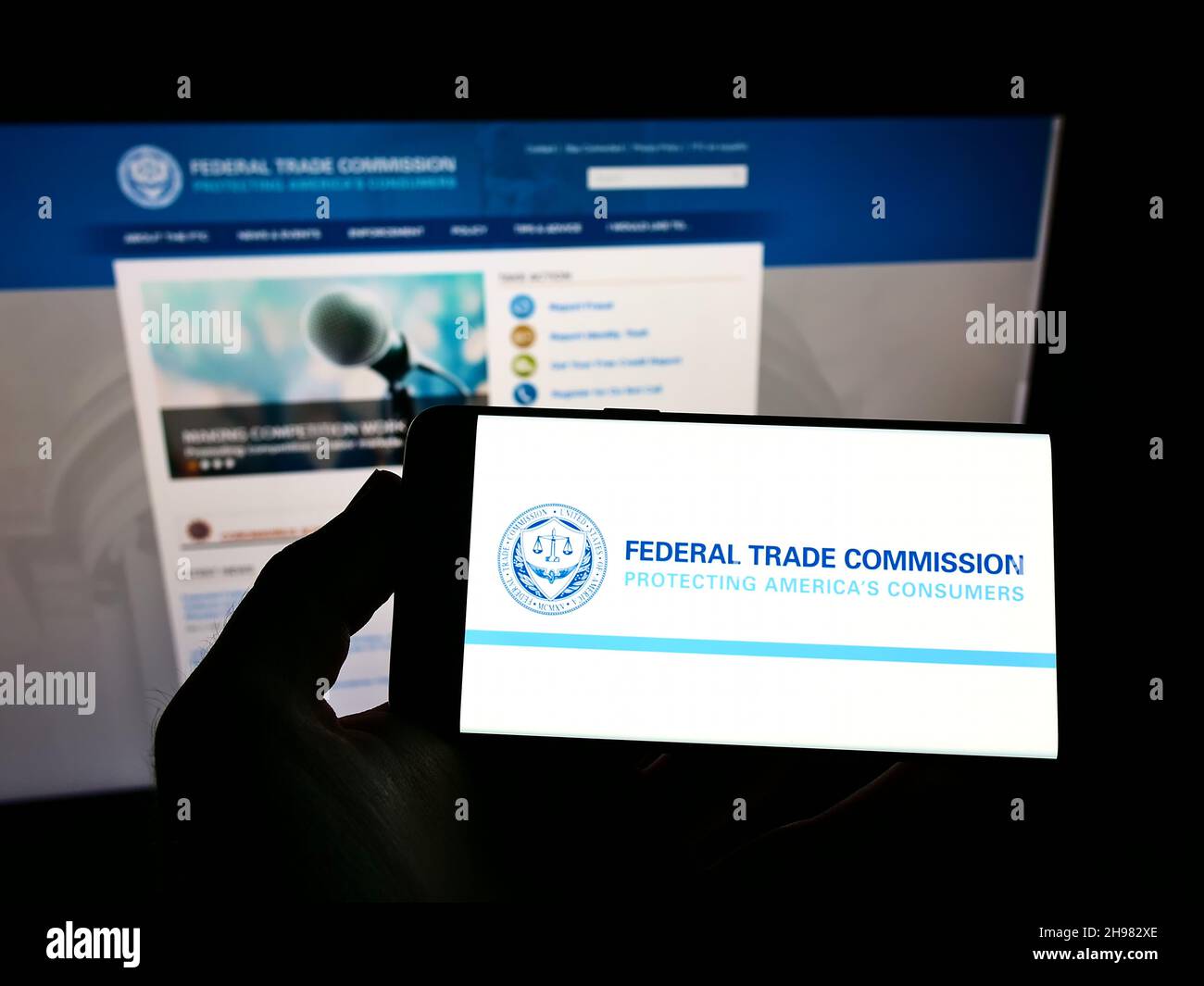 Persona che tiene uno smartphone con il logo dell'agenzia governativa statunitense Federal Trade Commission (FTC) sullo schermo di fronte al sito Web. Mettere a fuoco sul display del telefono. Foto Stock