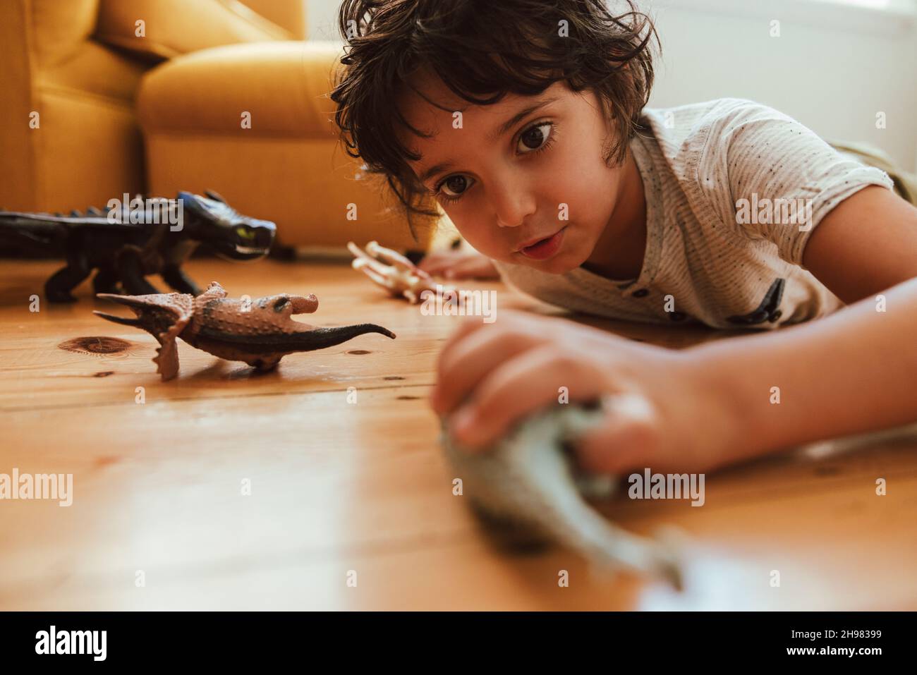 Ragazzino che gioca con i suoi giocattoli a casa. Adorabile ragazzo giovane che giace sul pavimento mentre gioca con giocattoli animali nella sua area gioco. Foto Stock