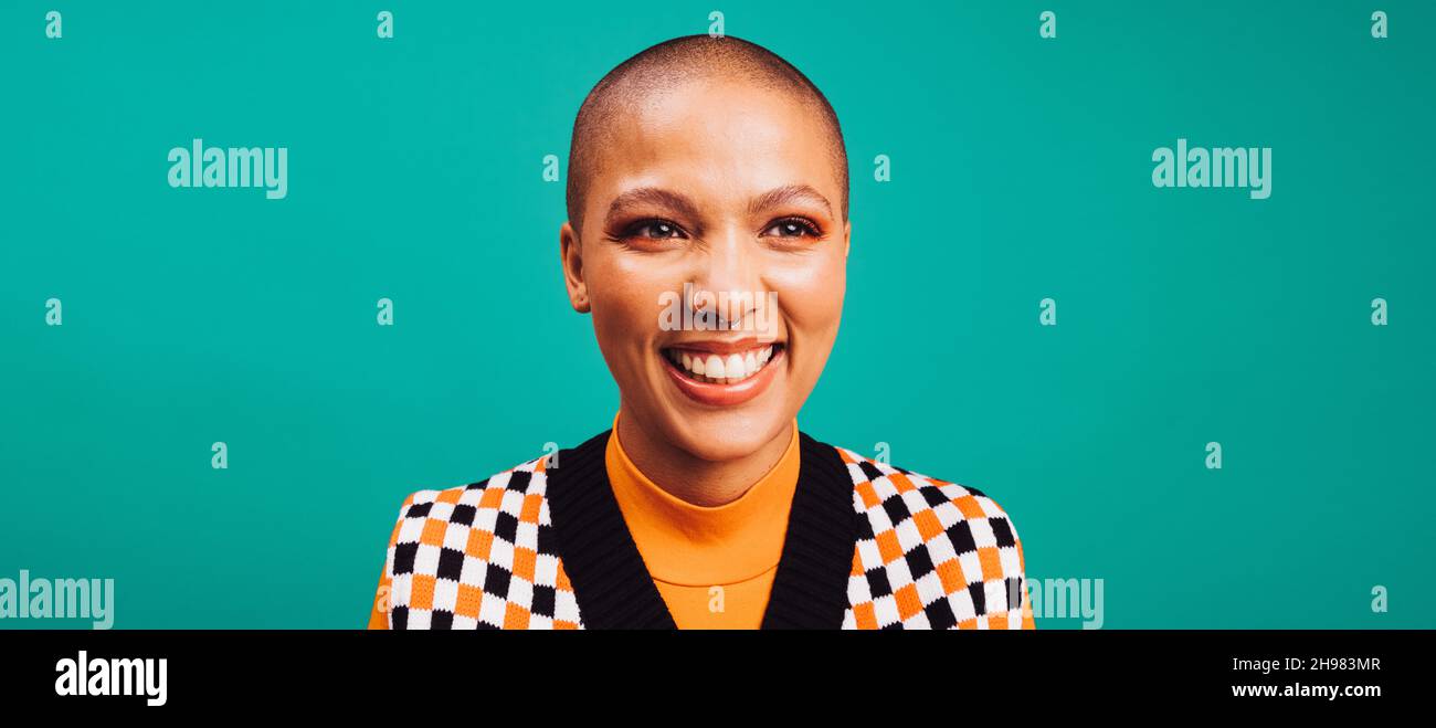 Donna dai capelli corti sorridente mentre si alza da sola contro uno sfondo turchese. Felice giovane donna che indossa un anello con setto in uno studio. Tassa donna hipster Foto Stock