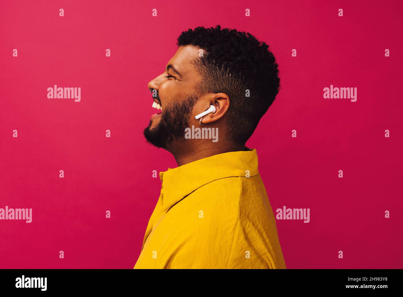 Ascoltare la mia musica preferita. Felice uomo giovane sorridente allegro mentre indossa le cuffie senza fili in uno studio. Spensierato giovane uomo in piedi da solo contro Foto Stock