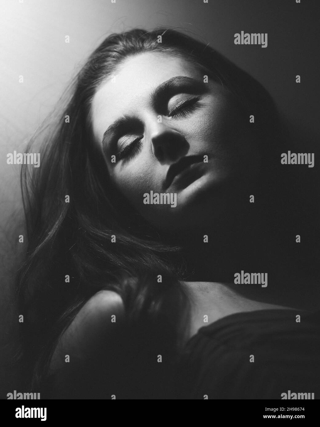 Un ritratto in scala di grigi di una donna di bruna melancholica che dorme sotto la luce Foto Stock