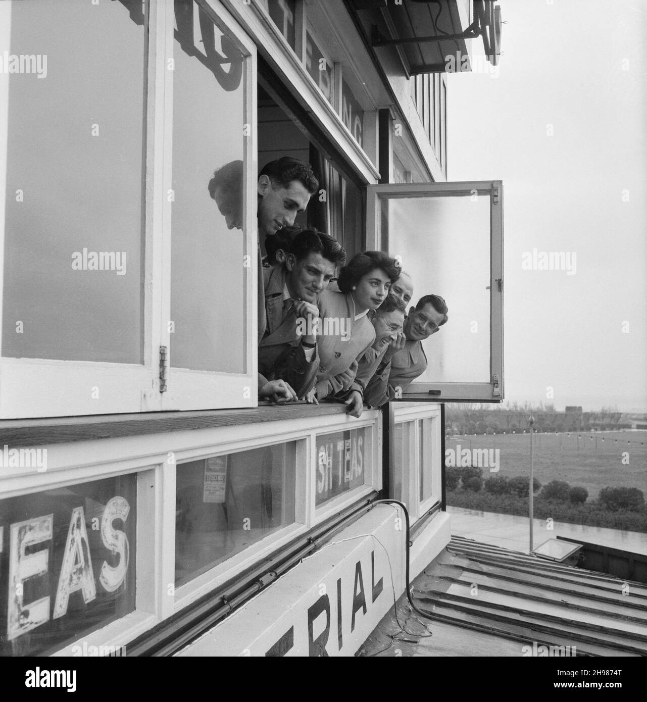 Imperial Cafe, Skegness, Skegness, East Lindsey, Lincolnshire, 22/05/1954. Un gruppo di uomini e una donna che si alzano dalla finestra al primo piano all'Imperial Cafe durante un viaggio del personale di Laing a Skegness. Nel 1947, dopo una pausa di sette anni, Laing aveva risuscitato le loro "uscite di zona" per il personale e le loro famiglie, con viaggi in maggio e giugno. Nel 1954 sono state previste sette uscite per cinque settimane a maggio e giugno. Questo viaggio a Skegness è stato per i dipendenti e le loro famiglie delle Midlands e del South Yorkshire. Una versione ritagliata di questa fotografia è stata pubblicata nel luglio 195 Foto Stock