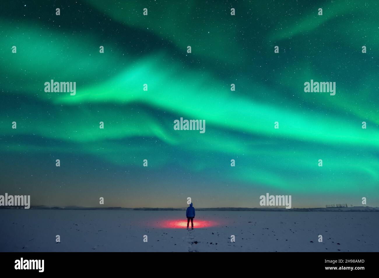 Turista con torcia rossa su campo nevoso sullo sfondo di incredibile cielo stellato con Aurora borealis. Panorama notturno incredibile. Aurora boreale in campo invernale Foto Stock
