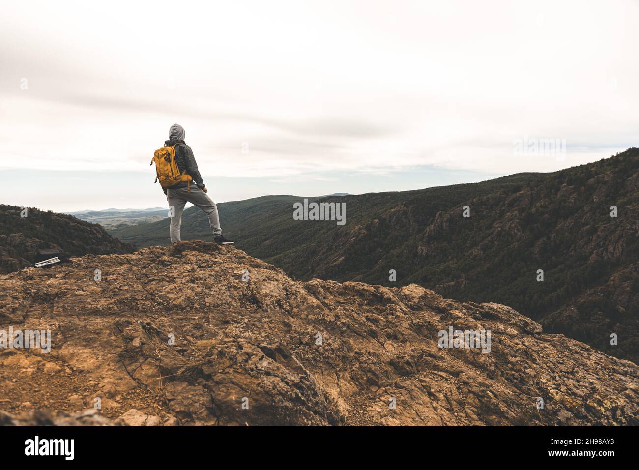 Un uomo in abiti da trekking con uno zaino giallo stand sulla cima di una collina tra le montagne intorno e sullo sfondo Foto Stock