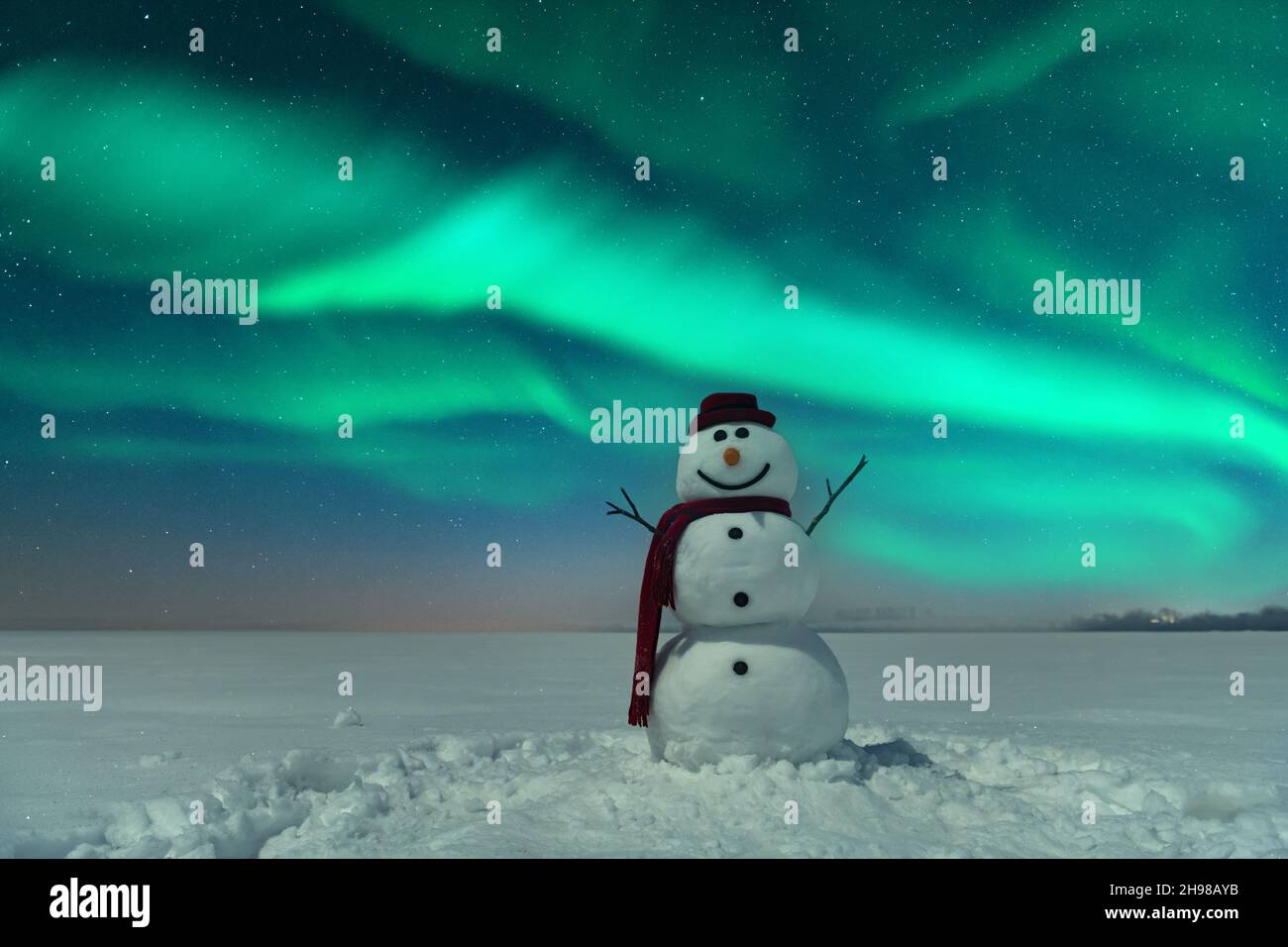 Divertente pupazzo di neve in elegante cappello rosso e cuoio capelluto rosso sul campo nevoso sullo sfondo di un incredibile cielo stellato con Aurora borealis. Panorama notturno incredibile. Aurora boreale in campo invernale Foto Stock