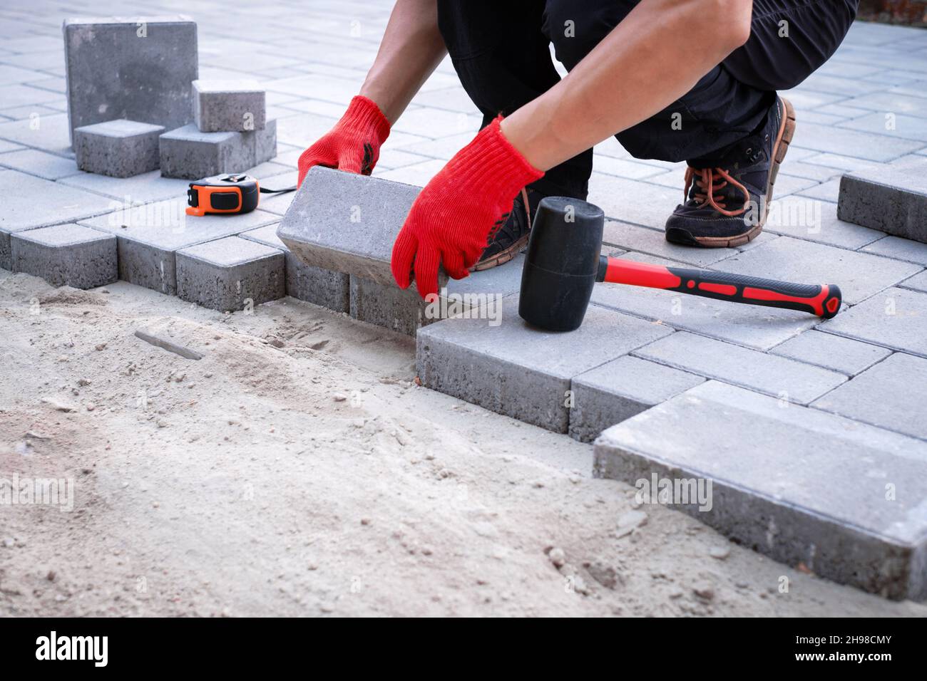 Il master in Guanti gialli getta pietre per pavimentazione in strati. Giardino percorso di mattoni da pavimentazione lastricatore professionale lavoratore. La posa di cemento grigio Pavimentazioni nel cortile della casa sulla sabbia foundation base. Foto Stock
