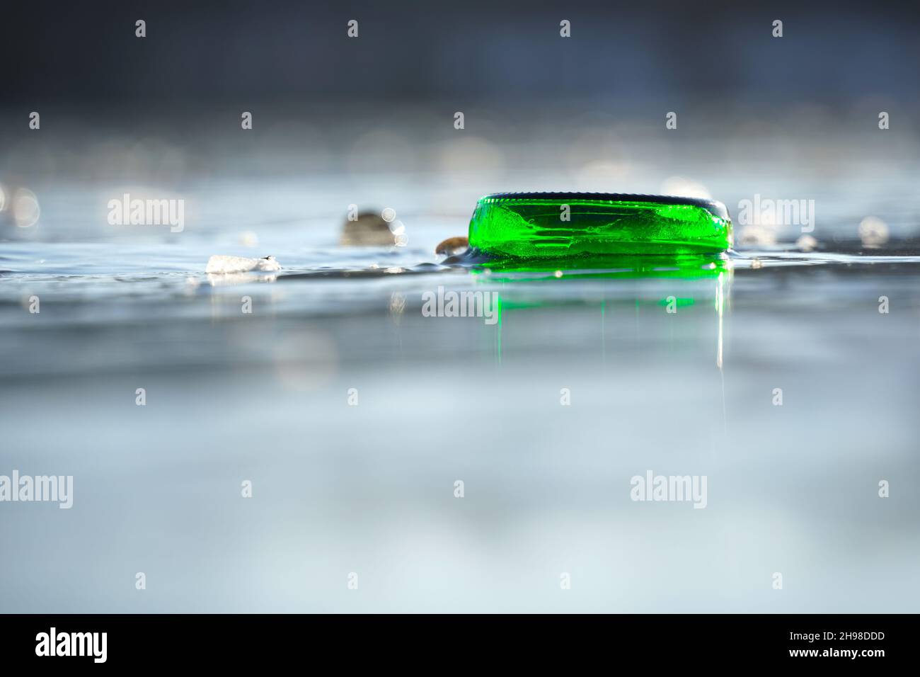 Il fondo della bottiglia verde è congelato solido nel lago. Piccole schegge di ghiaccio creano riflessi sulla superficie dell'acqua. Parte di un flacone. Vi. Anteriore Foto Stock