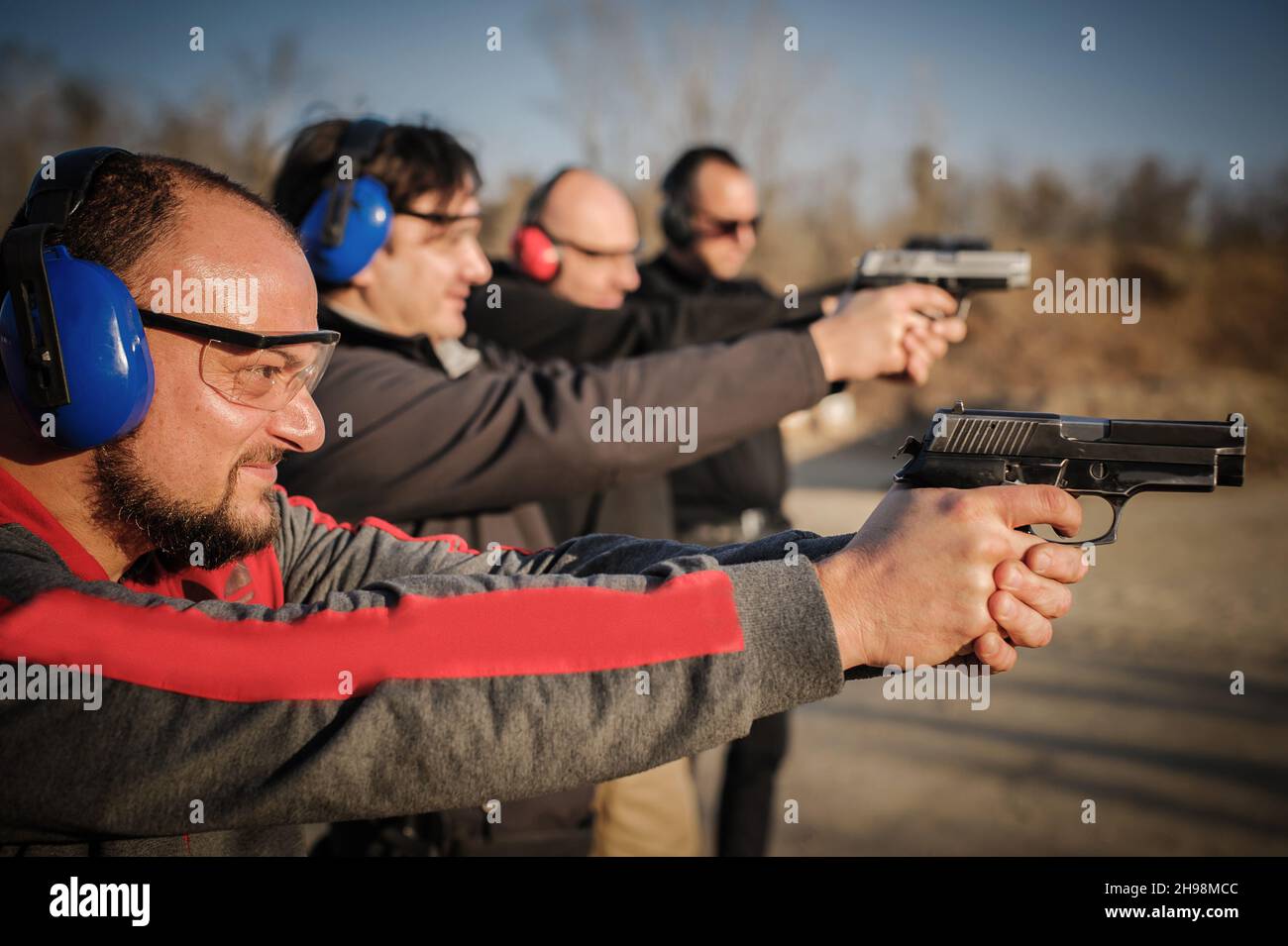 Gruppo di persone pratica sparare pistola su bersaglio su campo di tiro all'aperto. Addestramento delle armi della squadra civile Foto Stock