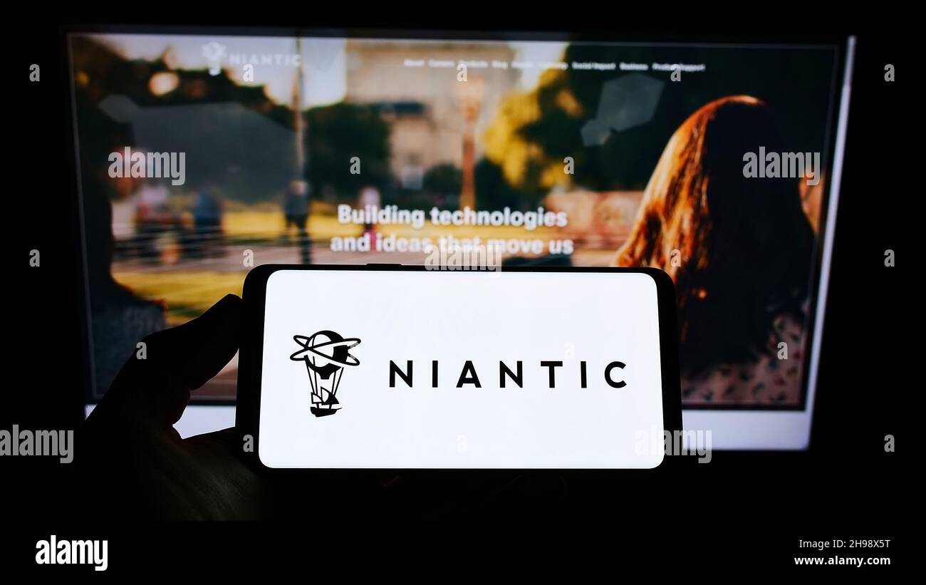 Persona che tiene uno smartphone con il logo della società statunitense di software di gioco Niantic Inc. Sullo schermo di fronte al sito web. Mettere a fuoco sul display del telefono. Foto Stock