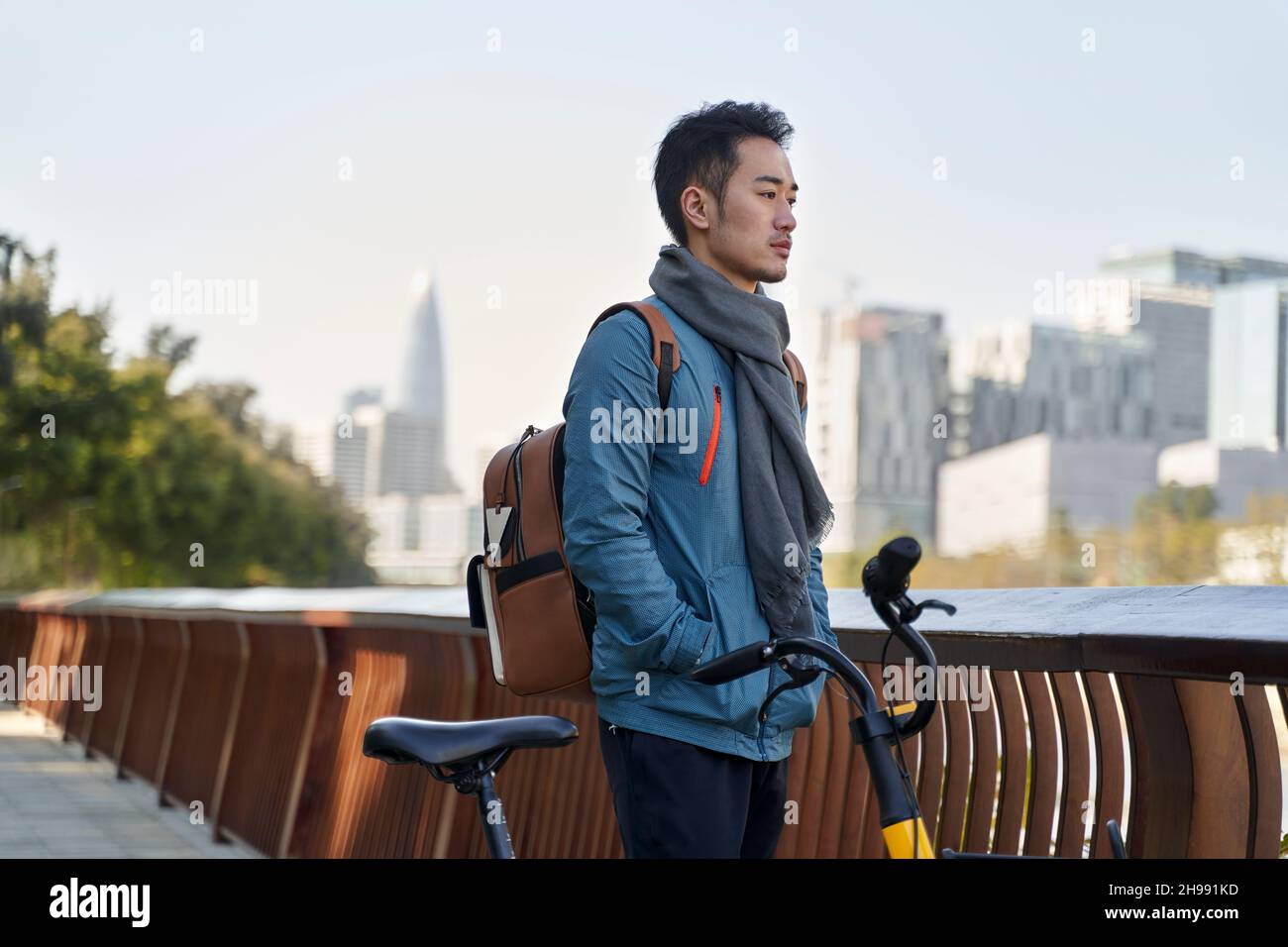 giovane uomo asiatico in piedi accanto a un fiume nel parco pubblico accanto a una bicicletta che pensa contemplare Foto Stock