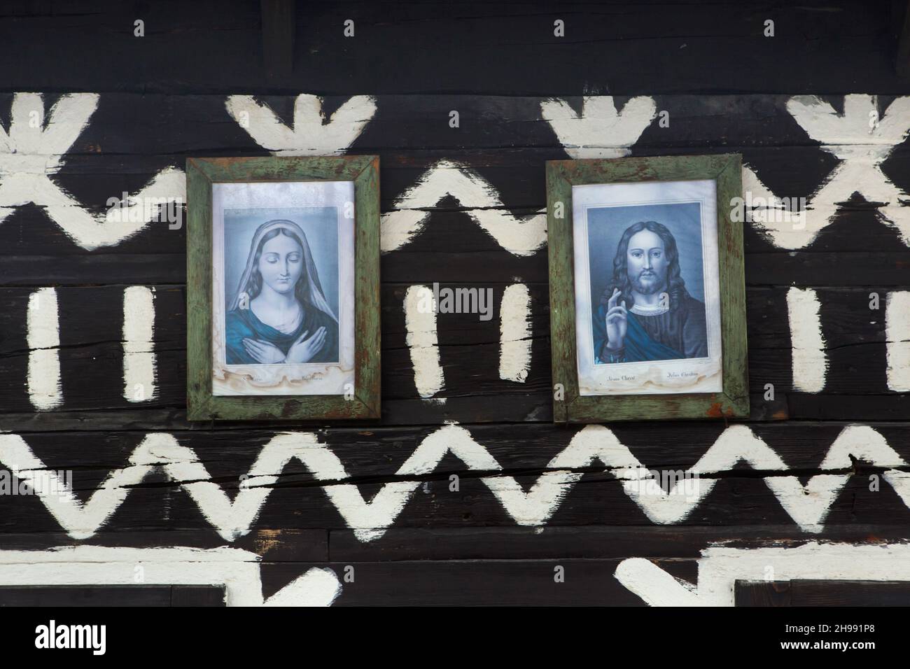 Immagini di Gesù Cristo e della Vergine Maria collocate nella tradizionale casa di tronchi decorata con motivi lineari bianchi nel villaggio di Čičmany nella regione di Žilina in Slovacchia. Foto Stock