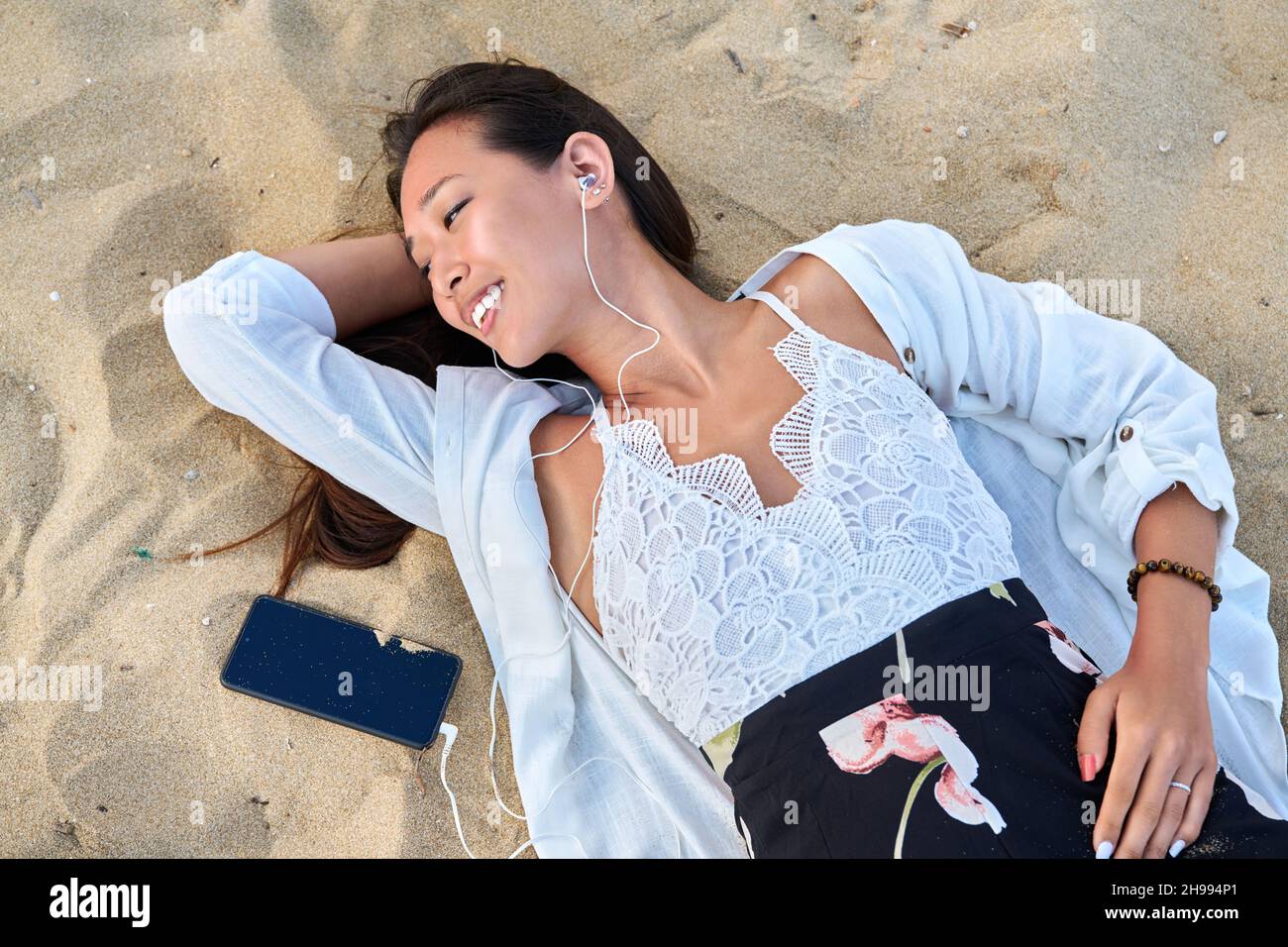 Una giovane donna rilassante in cuffie con smartphone sulla sabbia, vista dall'alto Foto Stock