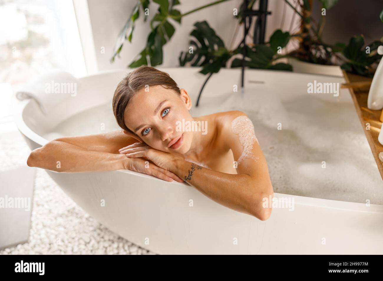 Bella giovane donna che si sente stanca, appoggiata sul lato della vasca da bagno, mentre si fa il bagno rilassante al centro benessere Foto Stock
