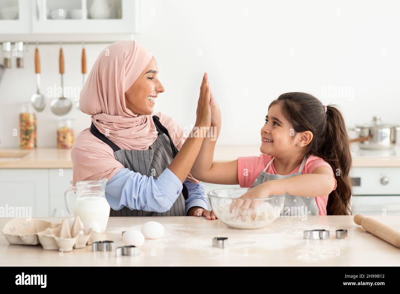 Felice mamma musulmana e figlia che danno High cinque mentre cottura in cucina Foto Stock