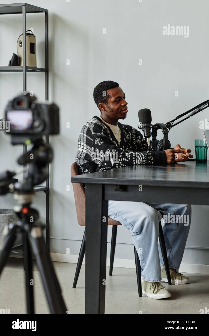 Ritratto verticale a tutta lunghezza del creatore afro-americano che parla al microfono mentre registra il podcast in studio Foto Stock