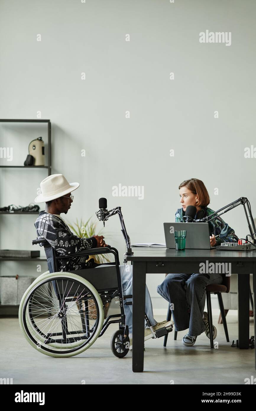 Ritratto verticale a tutta lunghezza di persona afro-americana con disabilità parlare al microfono mentre registra podcast in studio Foto Stock
