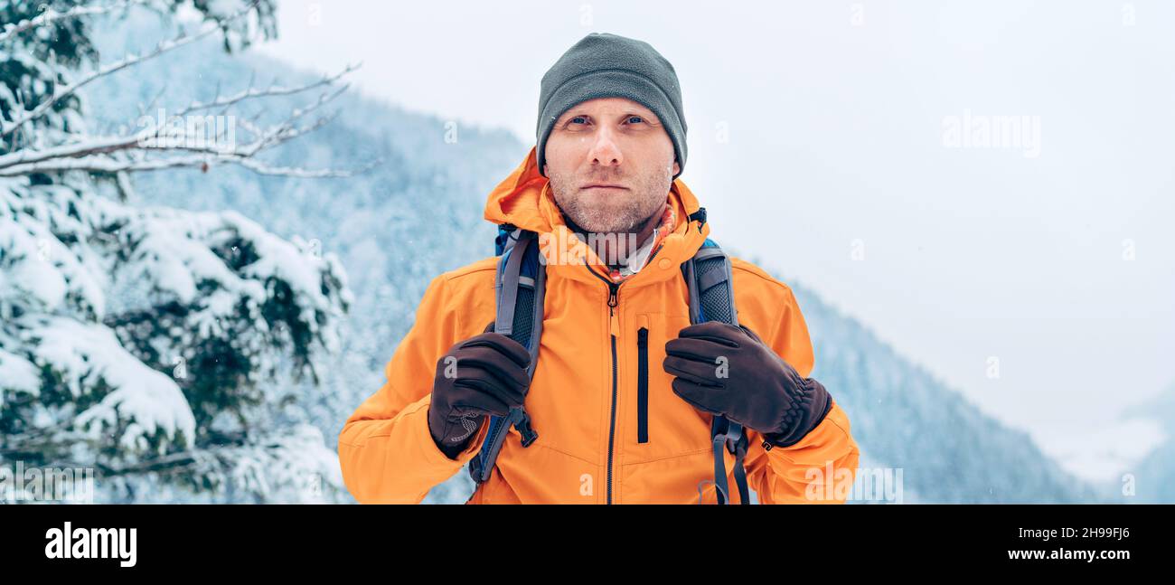 Giacca softshell arancione vestito da uomo con zaino, trekking lungo il percorso invernale delle montagne. Persone attive o sopravvivenza nel concetto di natura Foto Stock