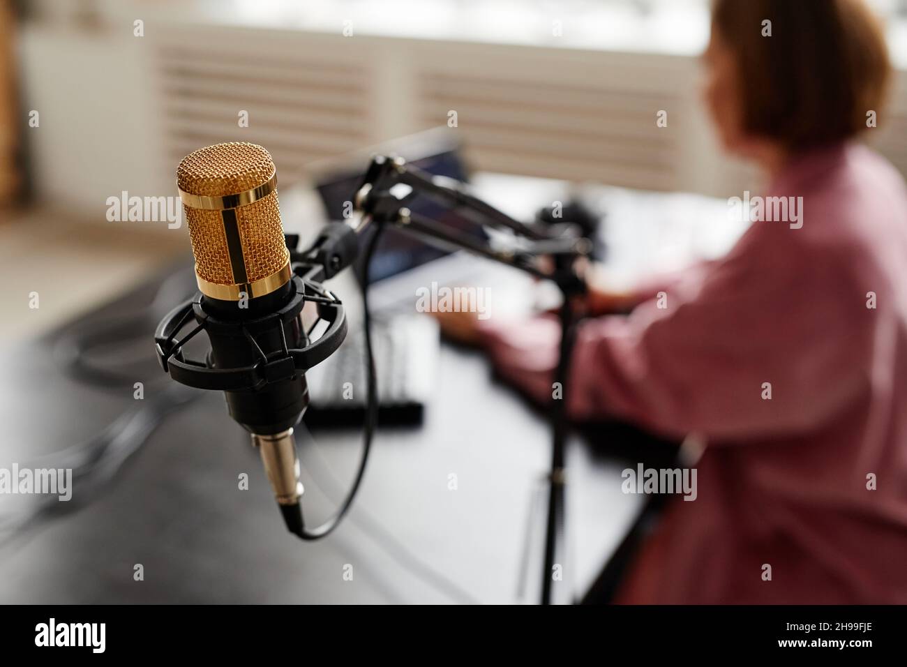 Primo piano del microfono da studio con il creatore femminile che imposta l'apparecchiatura di registrazione in background, spazio di copia Foto Stock