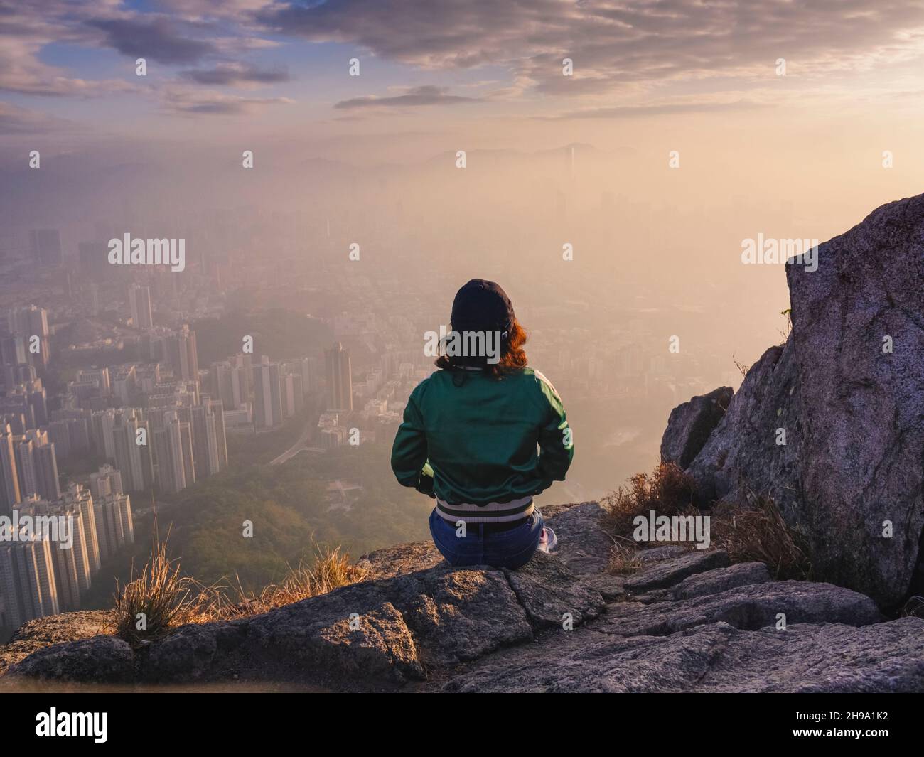 Donna seduta su roccia in colline sopra Hong Kong guardando giù sopra la città. Foto Stock