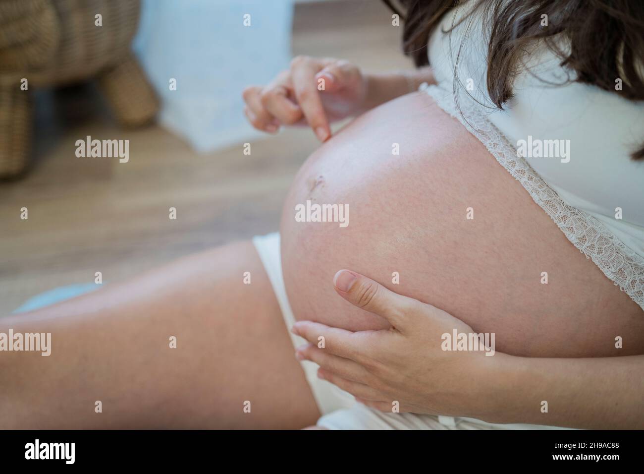 Donna incinta irriconoscibile che riposa sul pavimento e tocca delicatamente il ventre Foto Stock