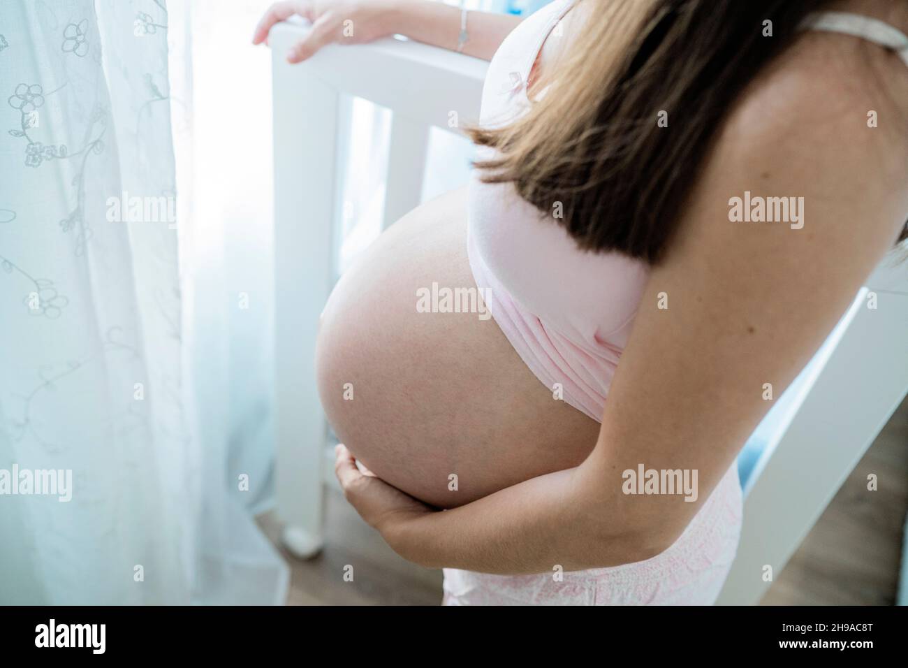 Donna incinta irriconoscibile che tocca il pancino nella stanza del bambino Foto Stock