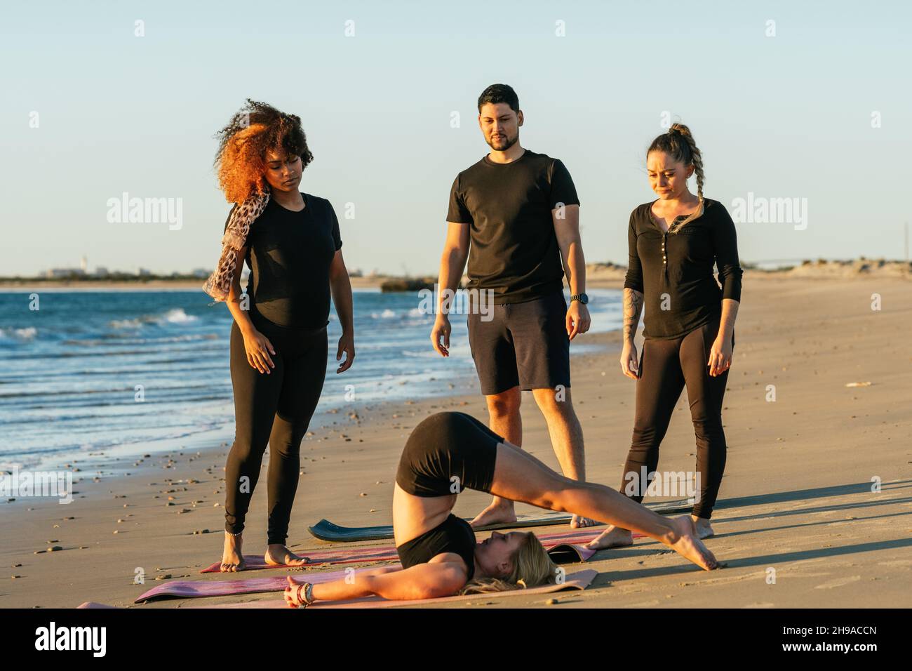 Allenatore di yoga che mostra una posa di yoga alla classe durante una sessione all'aperto Foto Stock