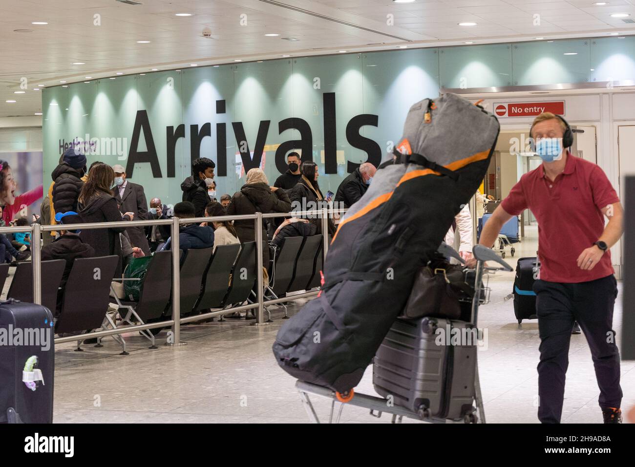 ,ale passeggero in t-shirt rossa spingere bagagli extra large nella sala degli arrivi dell'aeroporto di Londra Heathrow in mezzo a Omicron spread, Inghilterra Regno Unito Foto Stock