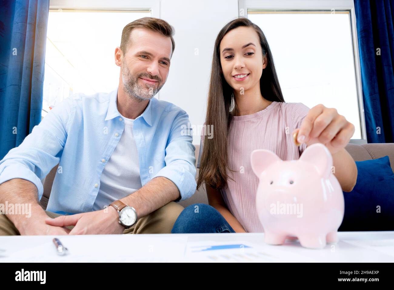 Mano che mette la moneta alla banca del piggy. La giovane coppia sta risparmiando i soldi per la loro nuova sede. Foto Stock
