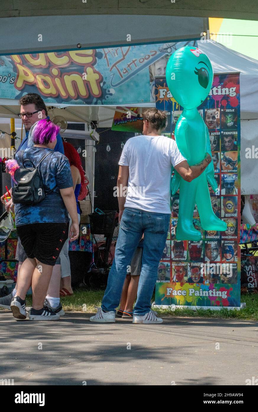 South Bend Indiana USA 4 luglio 2021; i fair-goers guardano intorno alla fiera della contea, e un uomo porta un enorme alieno colpo su ha vinto in una partita di carnevale Foto Stock