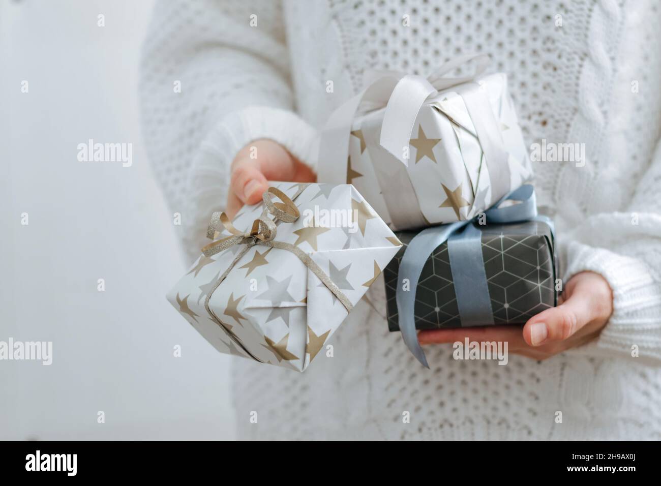 Una ragazza in maglione bianco contiene regali di festa. Le mani femminili stanno tenendo le scatole di festa. Il concetto di preparazione delle vacanze Foto Stock