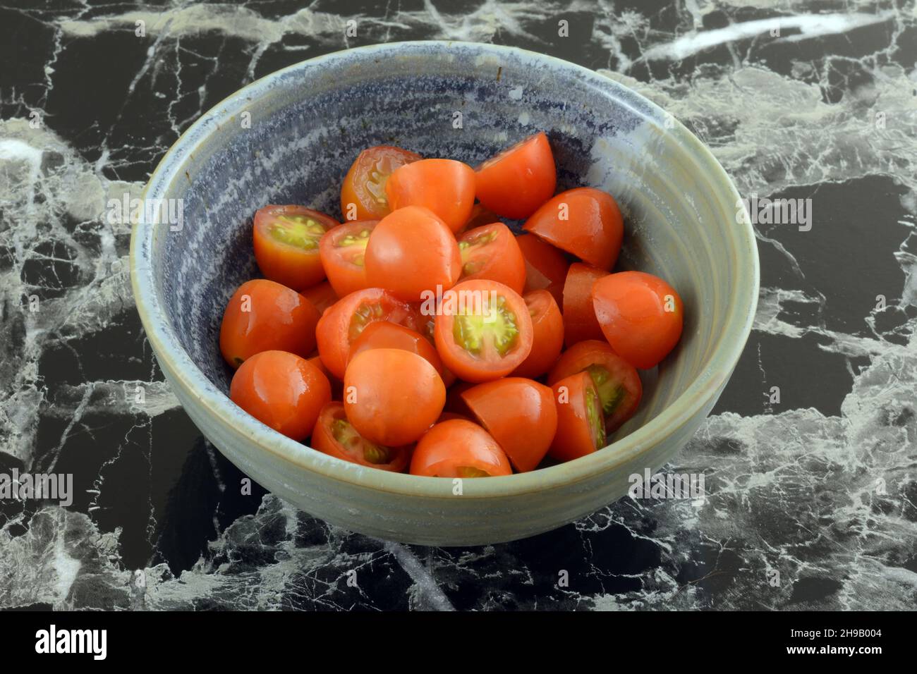 Metà del pomodoro fresco dell'uva cruda nel recipiente per ingredienti come preparazione per la cottura Foto Stock