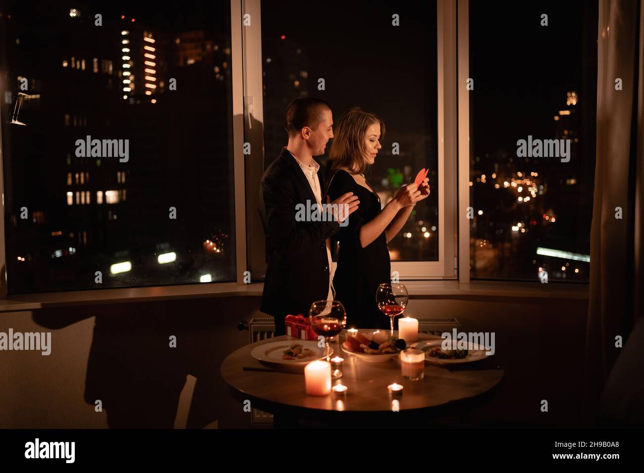 Coppia in amore festeggiando San Valentino cena con candele, anniversario o data di notte in un ristorante, finestre scure sfondo, uomo appassionato Foto Stock