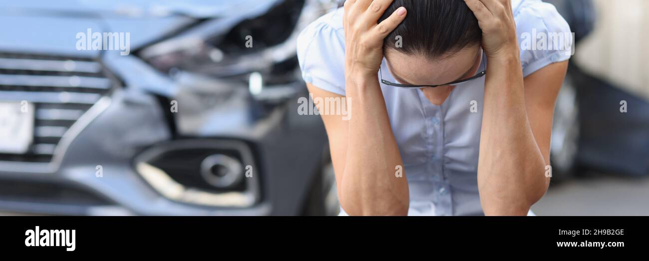 La donna spaventata si siede di fronte al closeup auto relitto Foto Stock