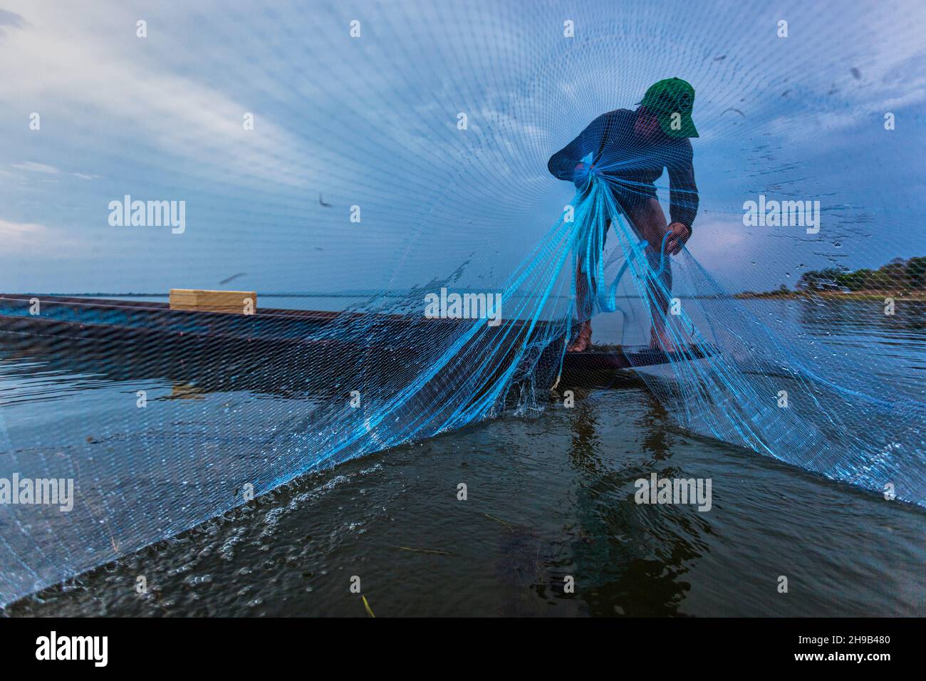 Pescatore in barca gettando rete nel fiume Foto Stock