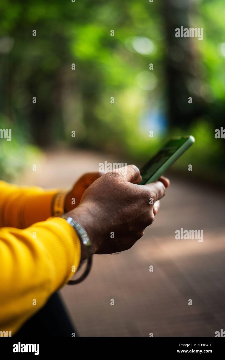 una persona che utilizza uno smartphone su sfondo verde bokeh, una mano maschio che tiene uno smartphone Foto Stock