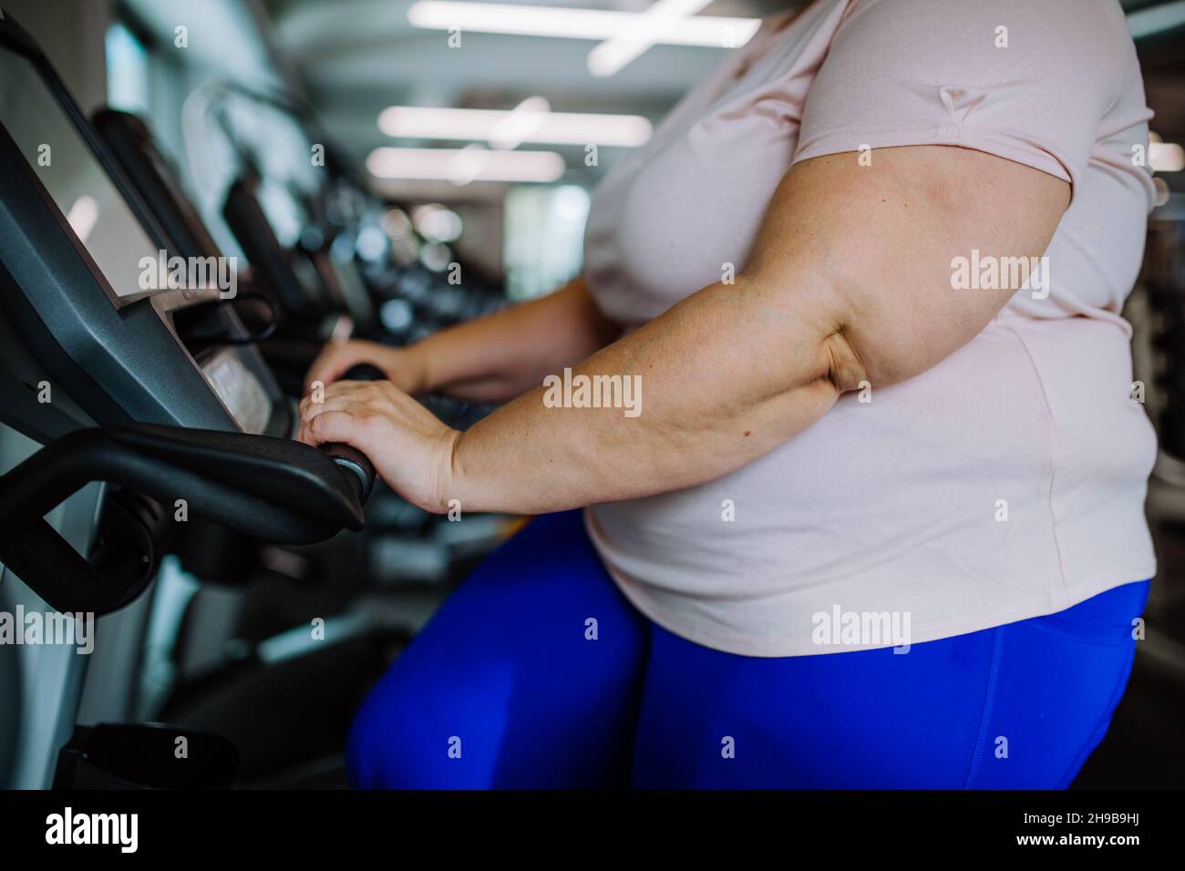 Metà sezione di donna sovrappeso che si esercita sul tapis roulant al coperto in palestra Foto Stock