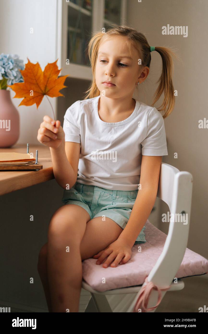 Vista ad angolo basso della bambina che tiene bella foglia di acero secco per creare l'erbario fai da te a casa. Foto Stock