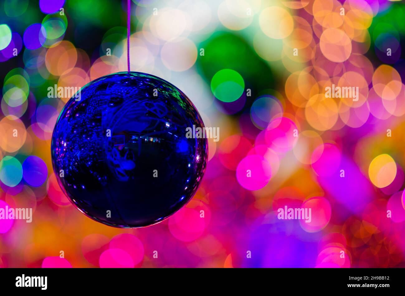 Bauble blu appeso a decorare per le vacanze di Natale con bokeh colorato dalla luce e altri baubles. Foto Stock