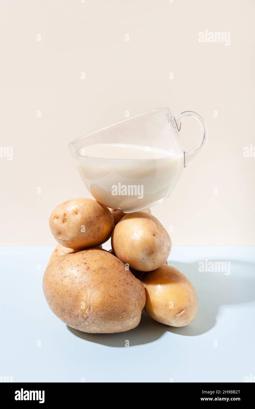 Latte vegetale alternativo. Composizione moderna con una tazza di latte di patate che si bilancia su un mucchio di patate. Foto Stock