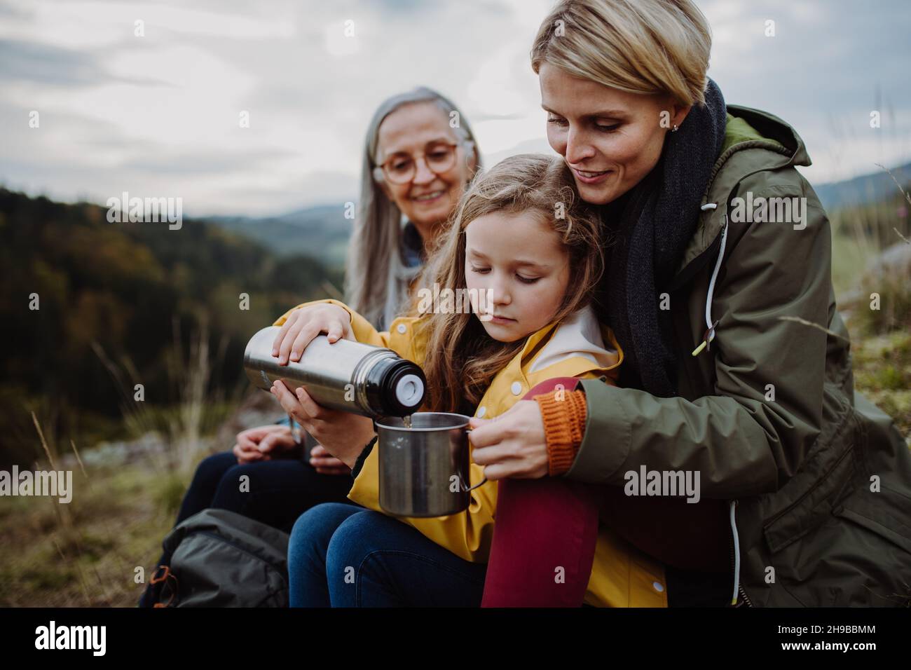 Bambina con madre e nonna seduta e versare il tè caldo sulla cima della montagna. Foto Stock