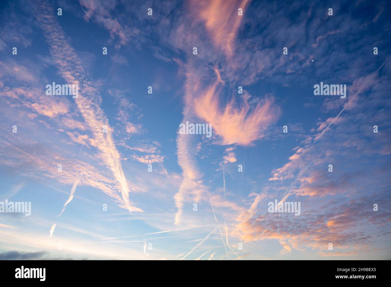 Formazioni di nubi spesse e percorsi di condensazione dall'aereo con il sole mattutino che illumina le nuvole e contrasta con una tinta arancione. Foto Stock