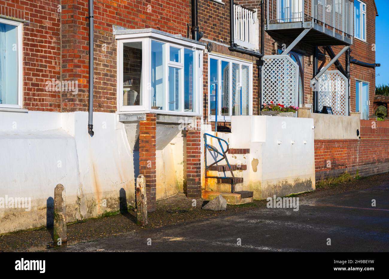 Edificio fronte mare con piano terra rialzato con gradini e muro di protezione su una strada che inonda ogni alta marea in Bosham Village, West Sussex, Regno Unito. Foto Stock