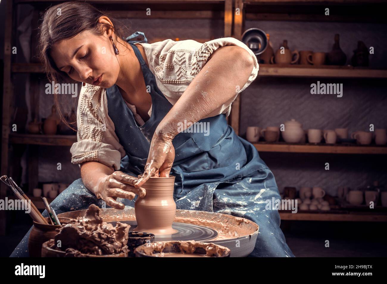 Affascinante maestro scultore artigiano lavora con argilla sulla ruota di un Potter e al tavolo con gli strumenti. Produzione artigianale. Foto Stock