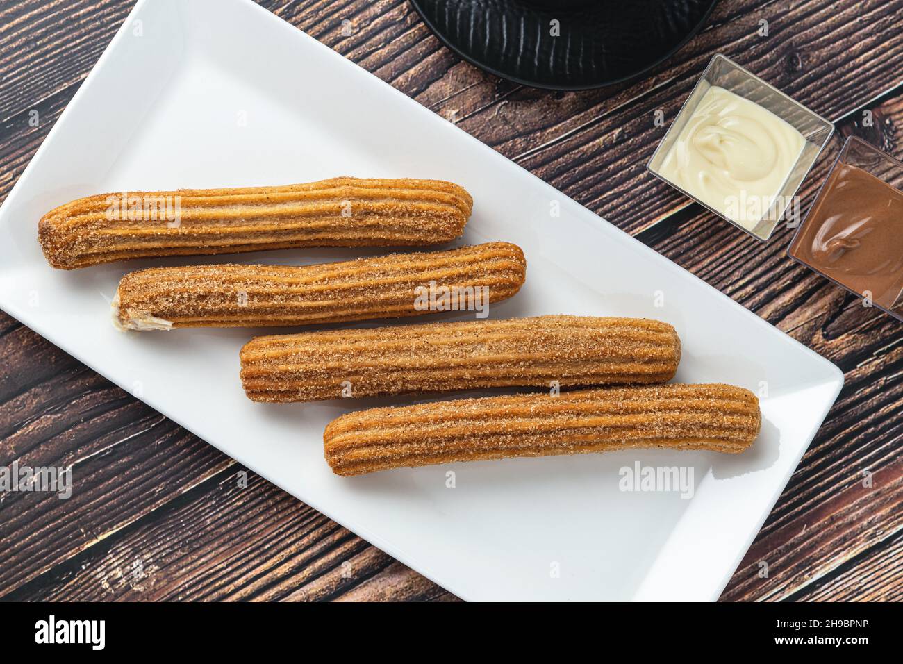 Churros caldi con salsa di cioccolato su tavola di legno. Foto Stock