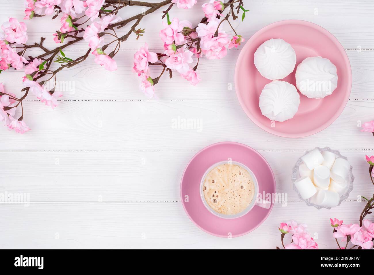 Tazza di caffè e marshmallows al mattino per colazione. Fiori di primavera e dessert su sfondo bianco di legno. Telaio. Modello con spazio di copia. P Foto Stock