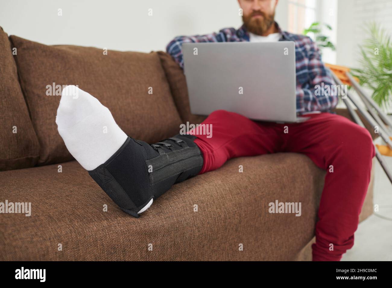 Un uomo ferito con gambe rotte sul laptop a casa Foto Stock