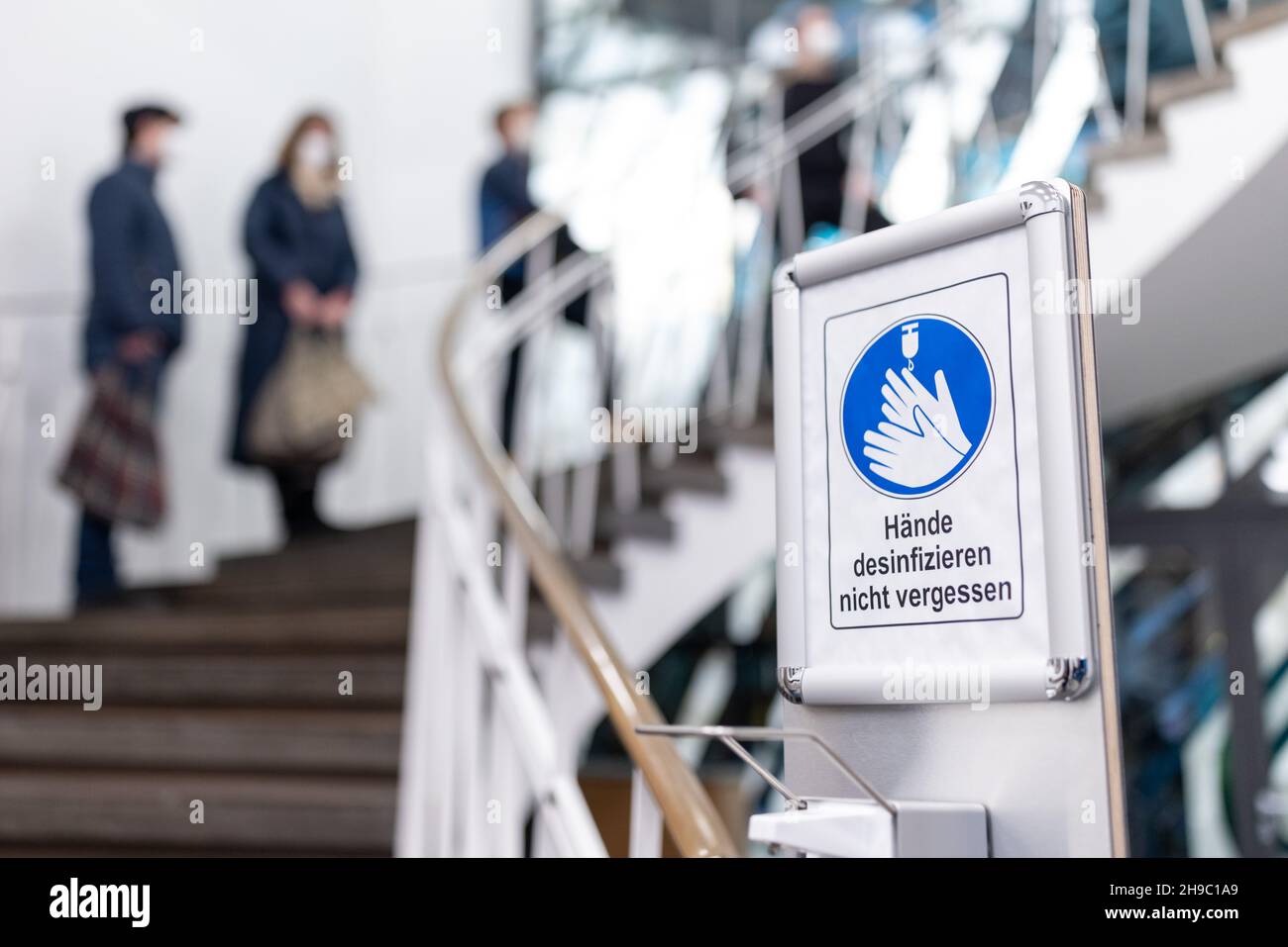 Norimberga, Germania. 06 dicembre 2021. "Non dimenticare di disinfettare le mani" è scritto su un cartello di fronte a un distributore di disinfettanti, davanti a una fila di persone in attesa nel nuovo centro di vaccinazione della camera di commercio di Norimberga. Credit: Daniel Karmann/dpa/Alamy Live News Foto Stock