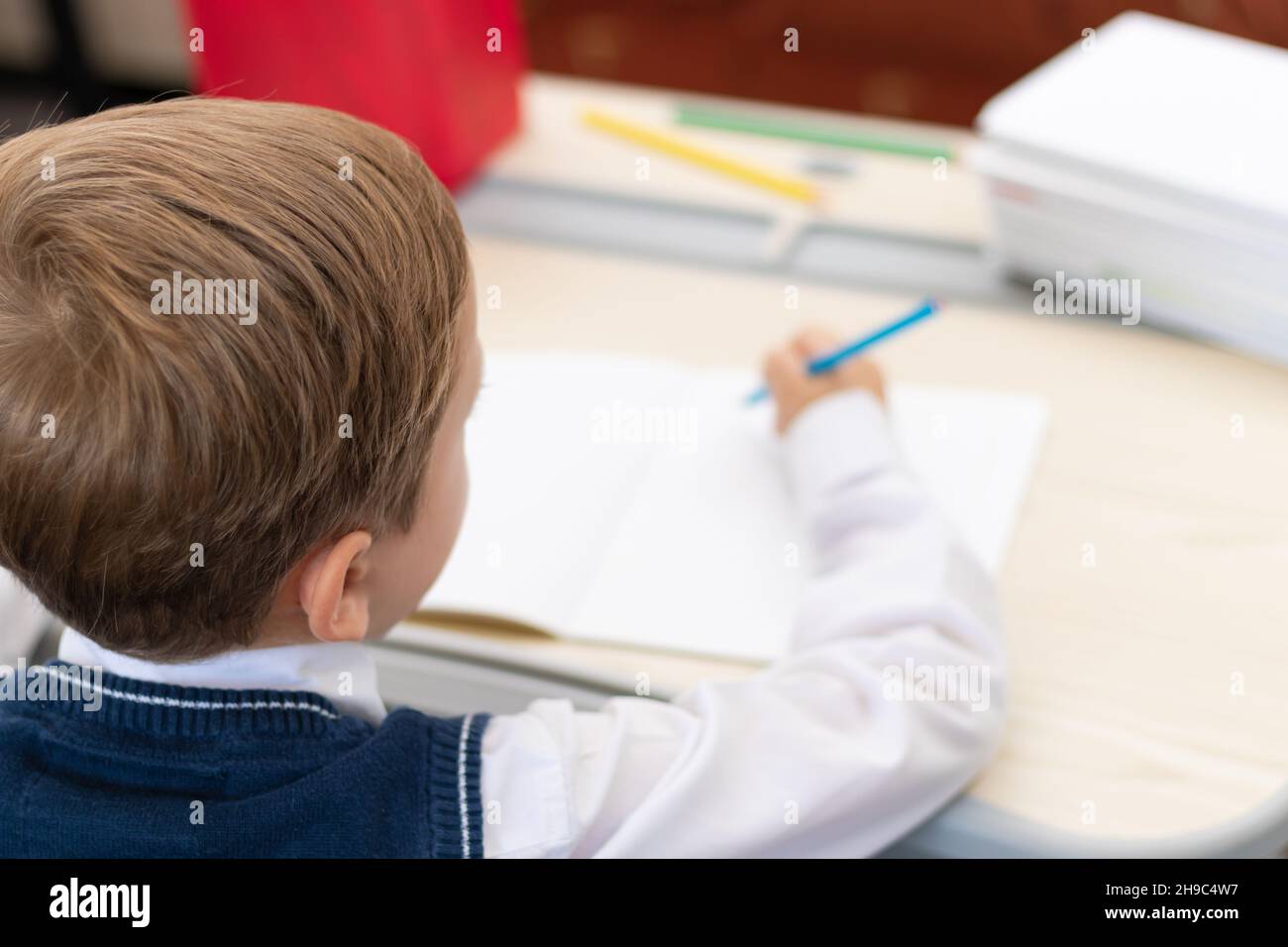 Un ragazzo carino prima livellatrice in una divisa della scuola fa i compiti mentre si siede ad una scrivania con una matita nelle sue mani a casa. Istruzione remota. Focu selettivo Foto Stock