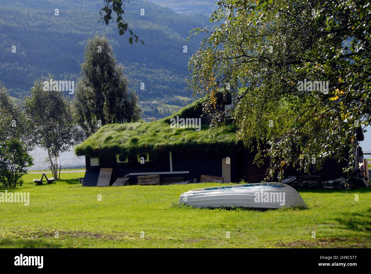 Edificio tradizionale sul lungomare con tetto in erba e barca capovolta accanto ad esso, Voss, Norvegia Foto Stock