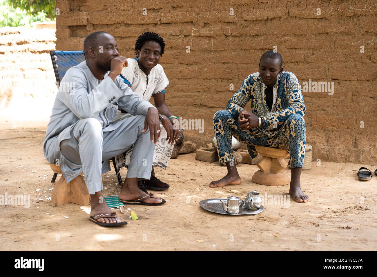 Tre abitanti neri africani condividono una tazza di tè durante una serata conviviale siesta nel loro cortile Foto Stock